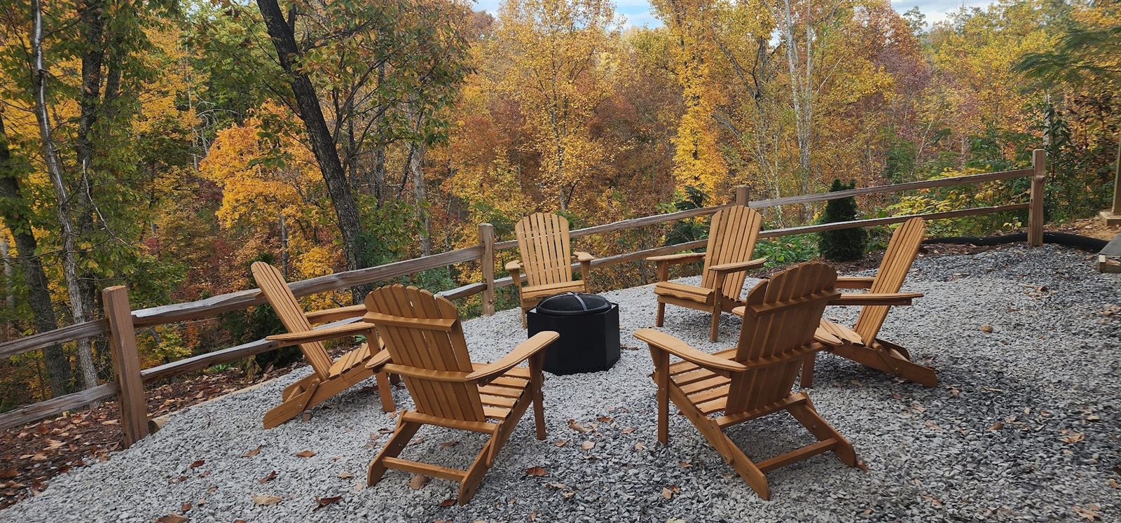 Adirondack chairs around the firepit with fall color behind